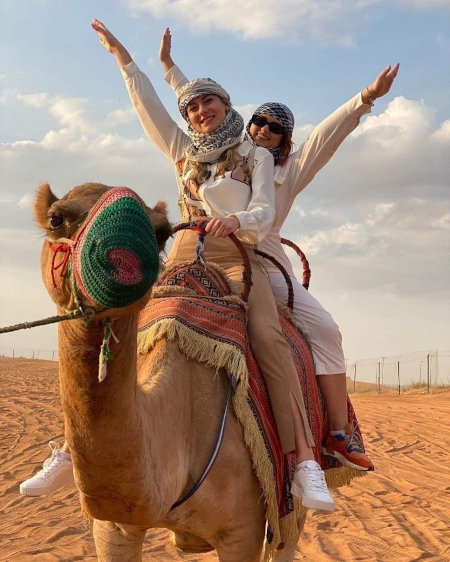 Two guests wearing traditional scarves on a camel in the desert